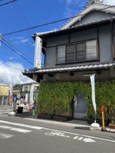 横河原のカドミセ前でアイスキャンデーを食べる子どもたちの様子。夏空の下、和風の建物と緑の蔦が印象的。