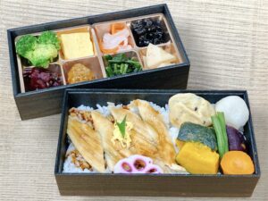 ごはんの上に香ばしい穴子の蒲焼きを乗せた二段弁当。彩り豊かな副菜とともに丁寧に盛り付けられている。