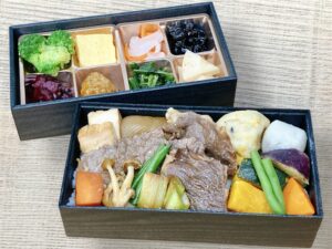 やわらかく煮込まれた牛肉や豆腐、野菜がごはんの上に盛られたすき焼き重。二段目には彩り豊かな副菜が詰め合わされている。