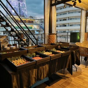 黒のテーブルクロスに並べられた華やかなビュッフェ料理と屋外会場の様子